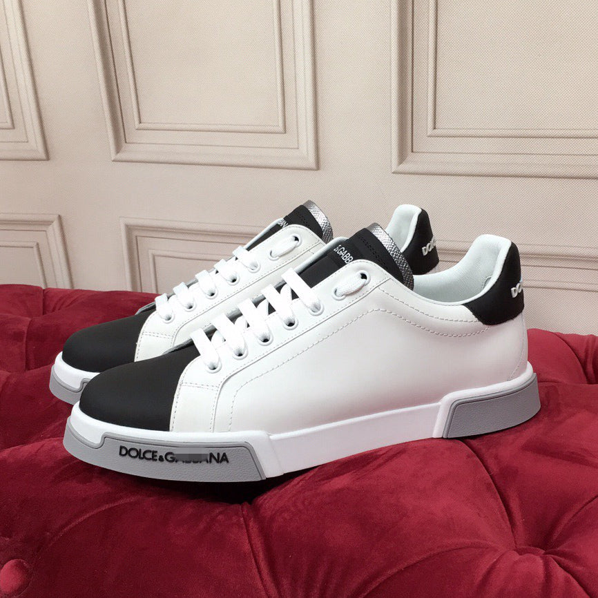 Two white low-top casual sneakers with black accent panels displayed on a red upholstered surface
